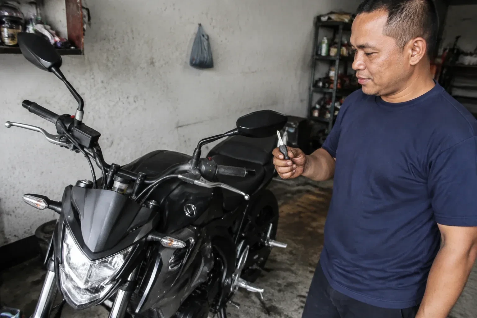 Person holding a key beside a black motorcycle in a garage. — Motorcycle & Scooter Keys, East Gwillimbury