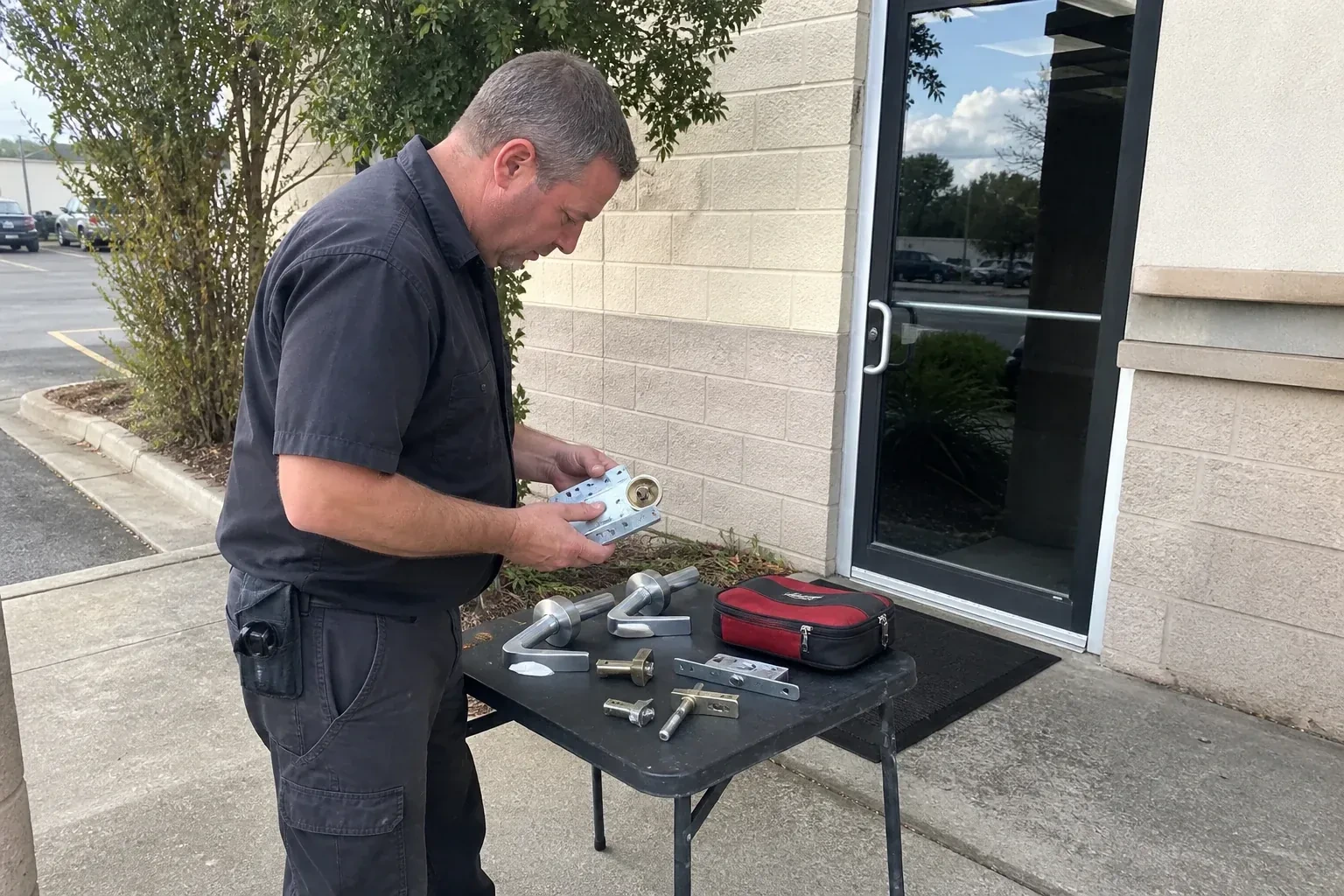 Technician examining detached commercial lock hardware on a table outside a shop entrance. — Business Lockout Service, East Gwillimbury