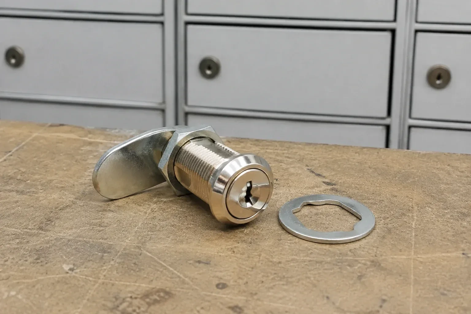 Detached threaded cam lock and mounting washer on a workbench in front of closed mail compartments. — Mailbox Lock Replacement, East Gwillimbury